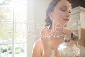 Beautiful bride applying perfume while standing by window
