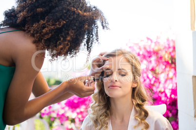 Side view of beautician applying mascara to bride