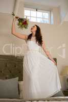 Beautiful bride holding bouquet singing while standing on bed at home