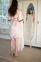 Smiling bride trying on dress while standing by mirror at home