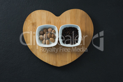 Nutmegs and black pepper seeds in heart shaped chopping board