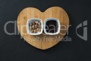 Nutmegs and black pepper seeds in heart shaped chopping board