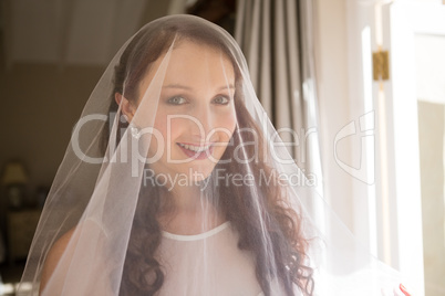 Portrait of happy bride in wedding dress standing by window