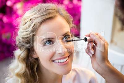 Cropped hand of woman applying mascara to smiling bride