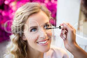 Cropped hand of woman applying mascara to smiling bride