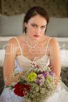 Portrait of sad bride with bouquet sitting on bed