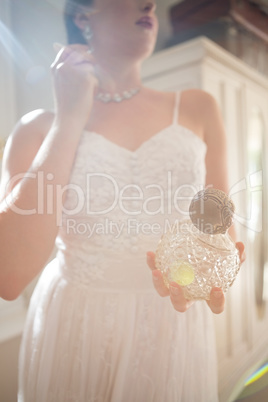Beautiful bride holding perfume while wearing earring at home