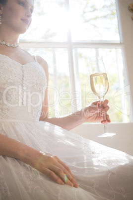 Low angle view of bride holding champagne while sitting by window