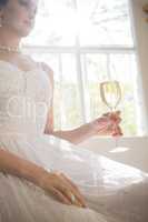 Low angle view of bride holding champagne while sitting by window