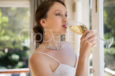 Bride looking through window while drinking champagne at home