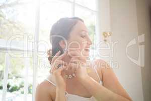 Beautiful bride wearing earring while standing by window