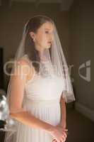 Thoughtful bride in wedding dress standing at home
