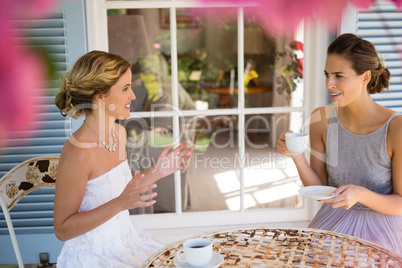 Happy bride and bridesmaid having coffee in yard