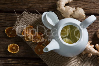 Lemon slice in teapot with ginger and dried orange on wooden table