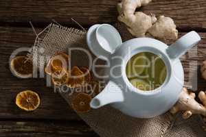 Lemon slice in teapot with ginger and dried orange on wooden table