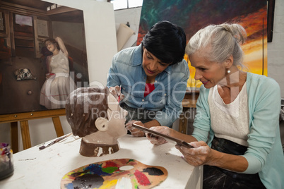 Woman using digital tablet while painting a sculptor