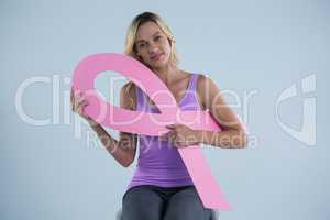 Portrait of young female sitting with cardboard Breast Cancer Awareness ribbon