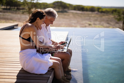 Couple using laptop near poolside