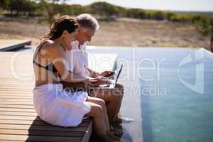 Couple using laptop near poolside