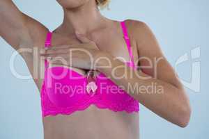 Mid section of woman in bra with Breast Cancer Awareness ribbon