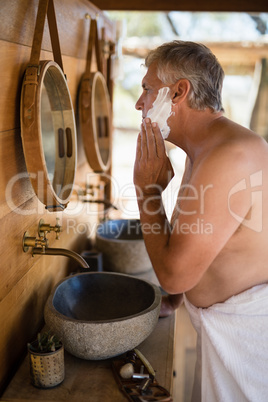 Man applying shaving cream on his face in cottage