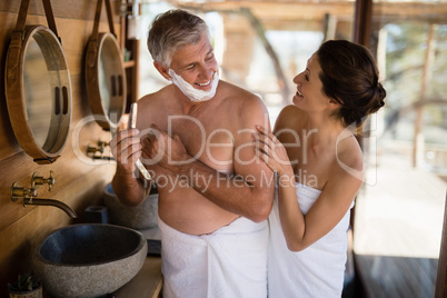 Smiling couple interacting while shaving in cottage