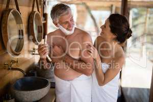 Smiling couple interacting while shaving in cottage