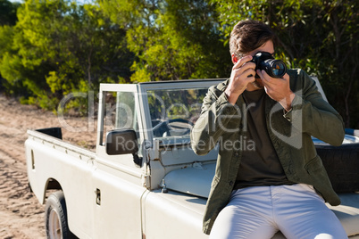 Man photographing while sitting on vehicle hood