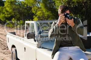 Man photographing while sitting on vehicle hood