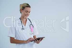 Smiling female doctor with Breast Cancer Awareness ribbon using tablet computer