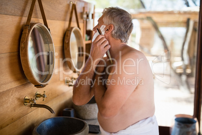 Man shaving his beard with razor in cottage