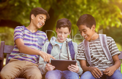 Composite image of boy with friends using digital tablet on bench