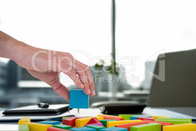 Composite image of cropped hand arranging colorful blocks