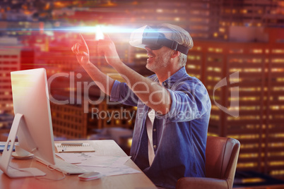 Composite image of businessman looking though virtual reality simulator while siting at desk