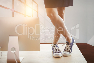 Composite image of low section of businesswoman standing on table by computer