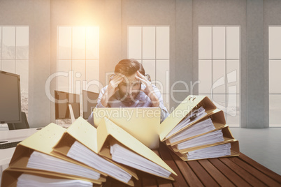 Composite image of frustrated businessman with head in hands sitting at desk