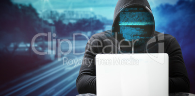 Composite image of hacker wearing black hood while using laptop on table