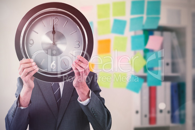 Composite image of businessman holding clock in front of his face