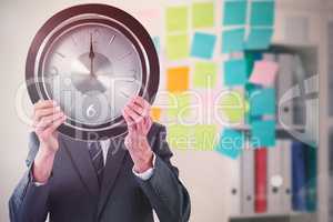 Composite image of businessman holding clock in front of his face
