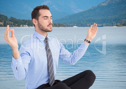 Business man meditating against river and hills with trees