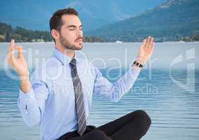 Business man meditating against river and hills with trees