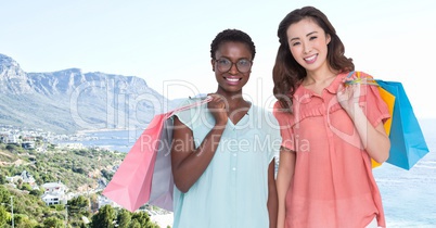 Millennial women with shopping bags against blurry coastline