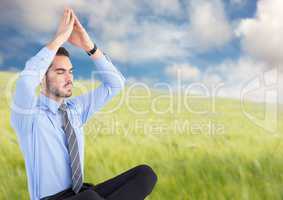 Business man meditating against blurry meadow
