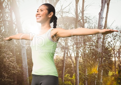 Woman arms outstretched against blurry trees with flare