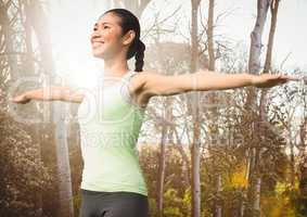 Woman arms outstretched against blurry trees with flare
