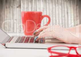 Hands with laptop and red coffee cup against blurry wood panel