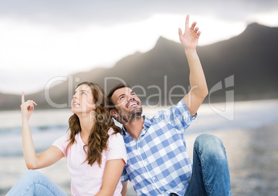 Couple sitting and pointing against blurry beach