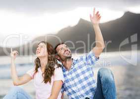 Couple sitting and pointing against blurry beach