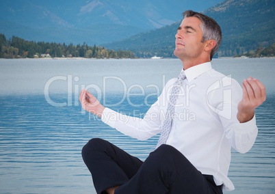 Business man meditating against water and hills