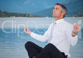 Business man meditating against water and hills